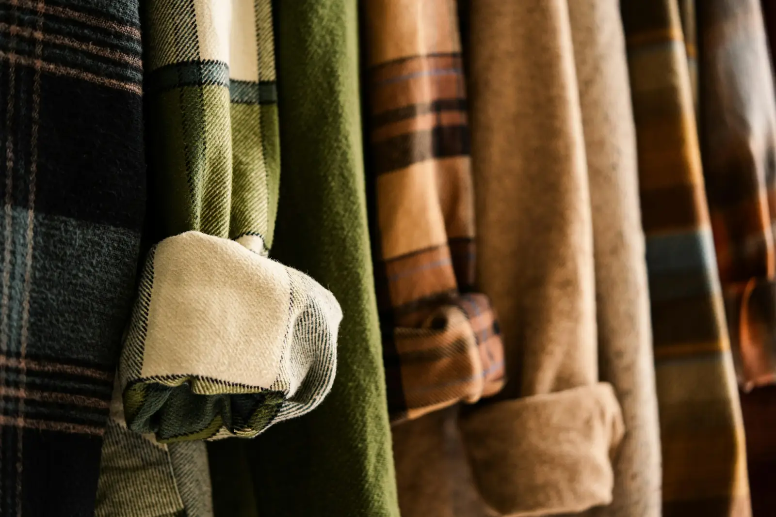 A rail of flannel and wool shirts in plaid, olive, brown and cream hanging close together