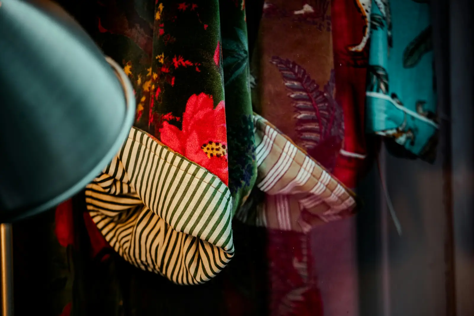 Rich patterned fabrics in deep green, red and striped designs hanging together on a rail