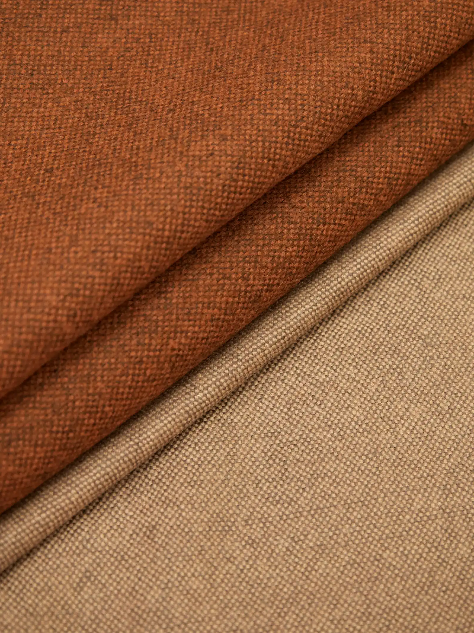 Two folded lengths of wool suiting fabric, one rust brown and one camel, laid diagonally