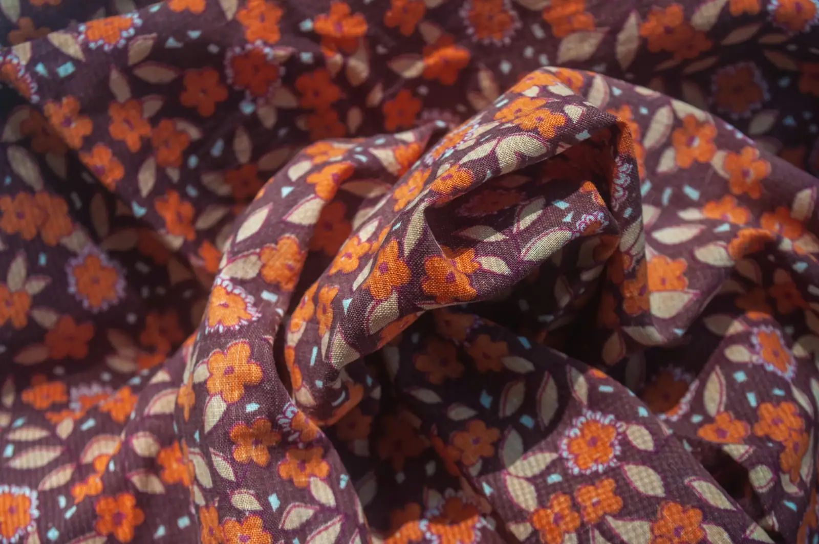 Crumpled cotton fabric printed with small orange and cream flowers on a deep plum background
