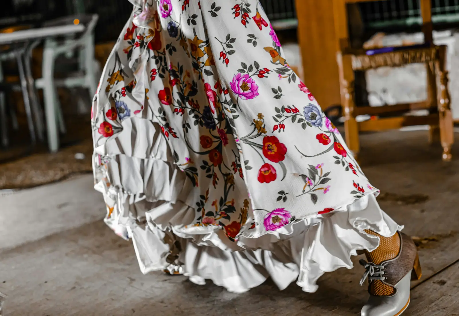 A woman in a flowing white skirt printed with red and pink roses walking across a wooden floor