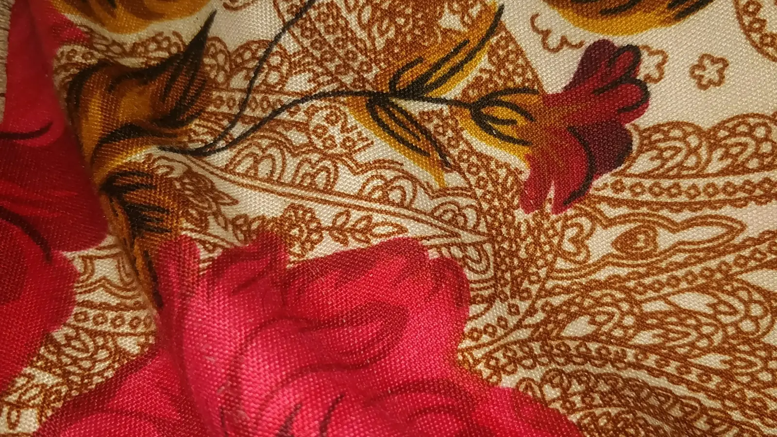 Close-up of cotton fabric printed with large red roses and brown paisley outlines on a cream ground