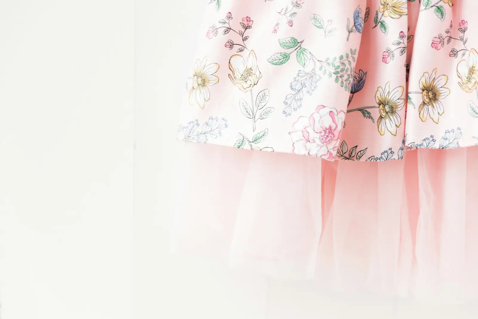The hem of a pale pink floral cotton skirt with small painted flowers and a tulle underlayer