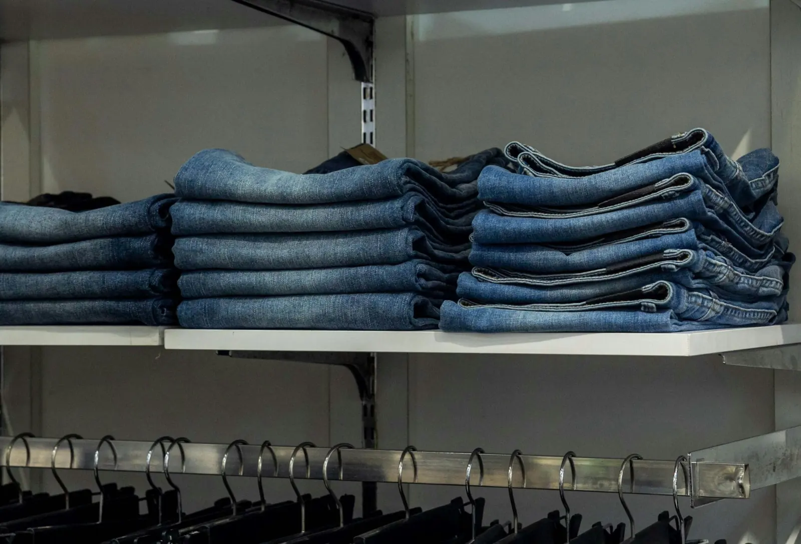 Stacks of folded blue jeans in several washes arranged on white shelves in a clothing store
