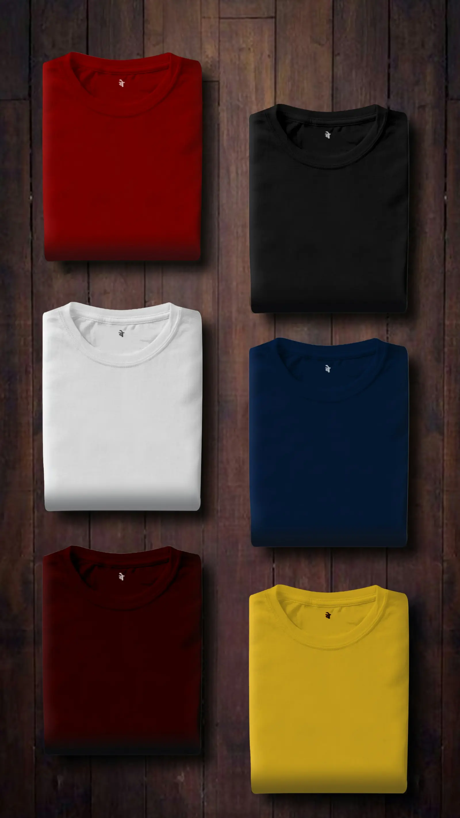 Six plain cotton T-shirts folded neatly in red, black, white, navy, maroon and yellow on a dark wooden surface