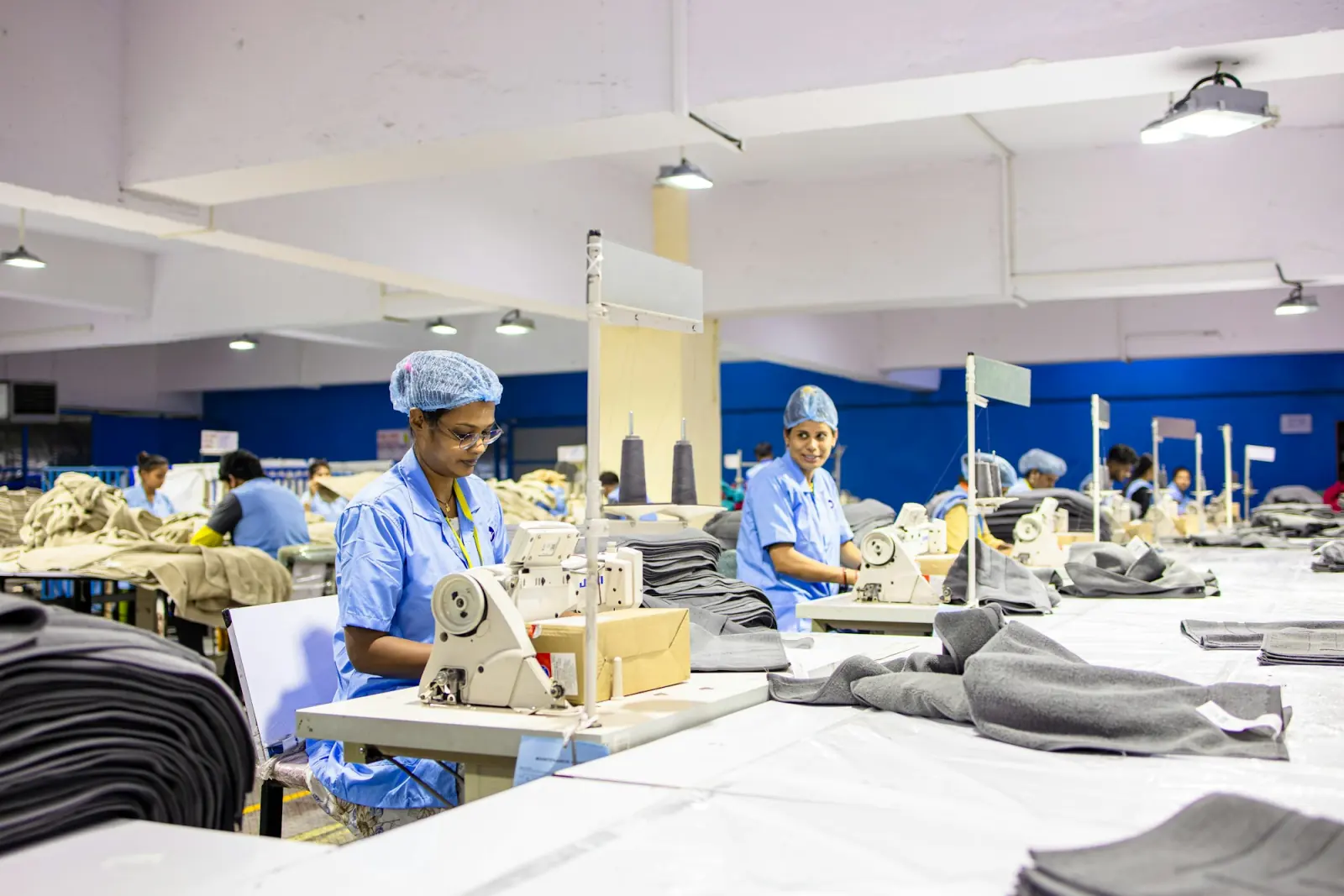 Rows of tailors in caps and uniforms working at industrial sewing machines in a large garment unit
