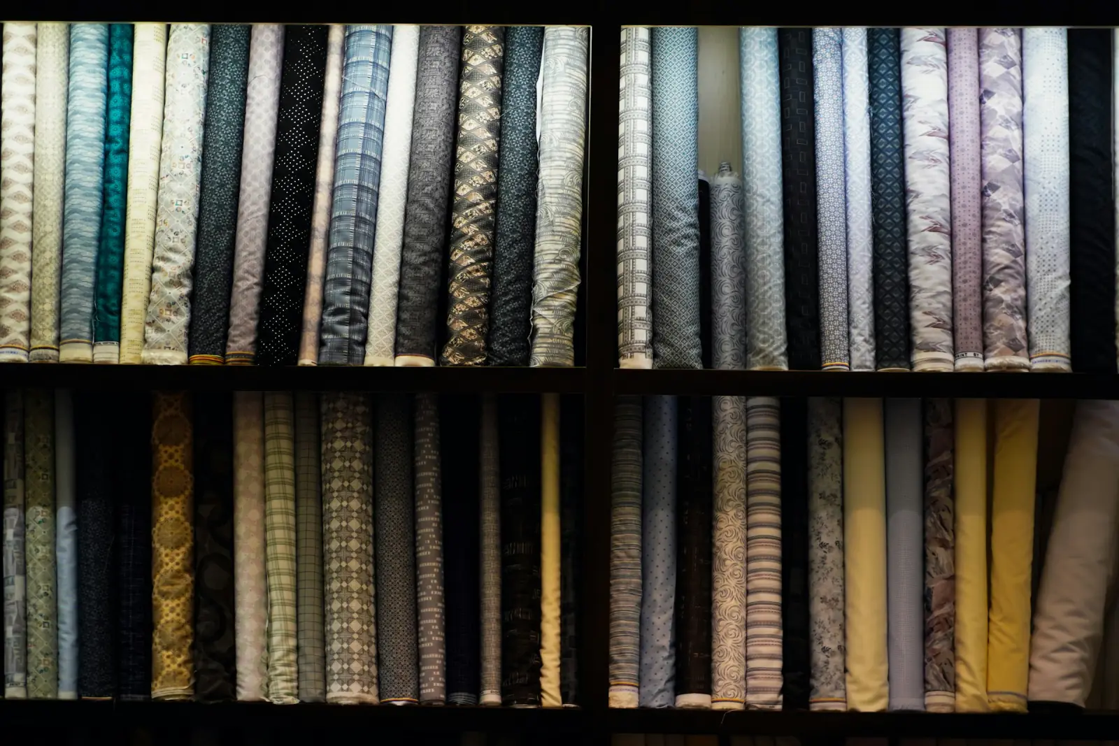 Floor-to-ceiling wooden shelves packed with rolls of patterned suiting and shirting fabric