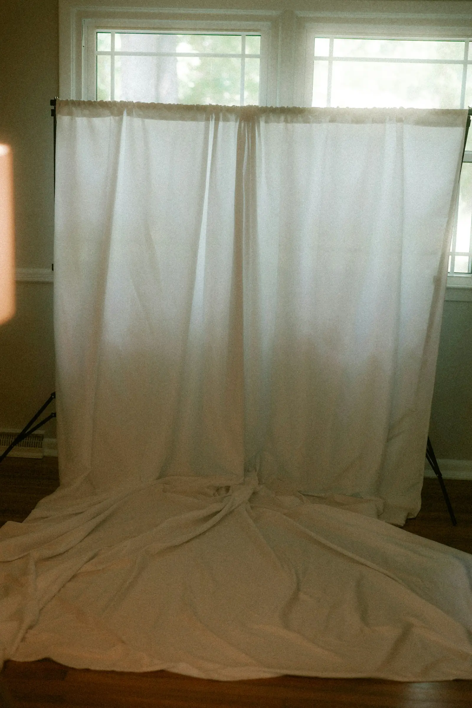 A length of white muslin fabric hung on a stand as a photography backdrop in a sunlit room