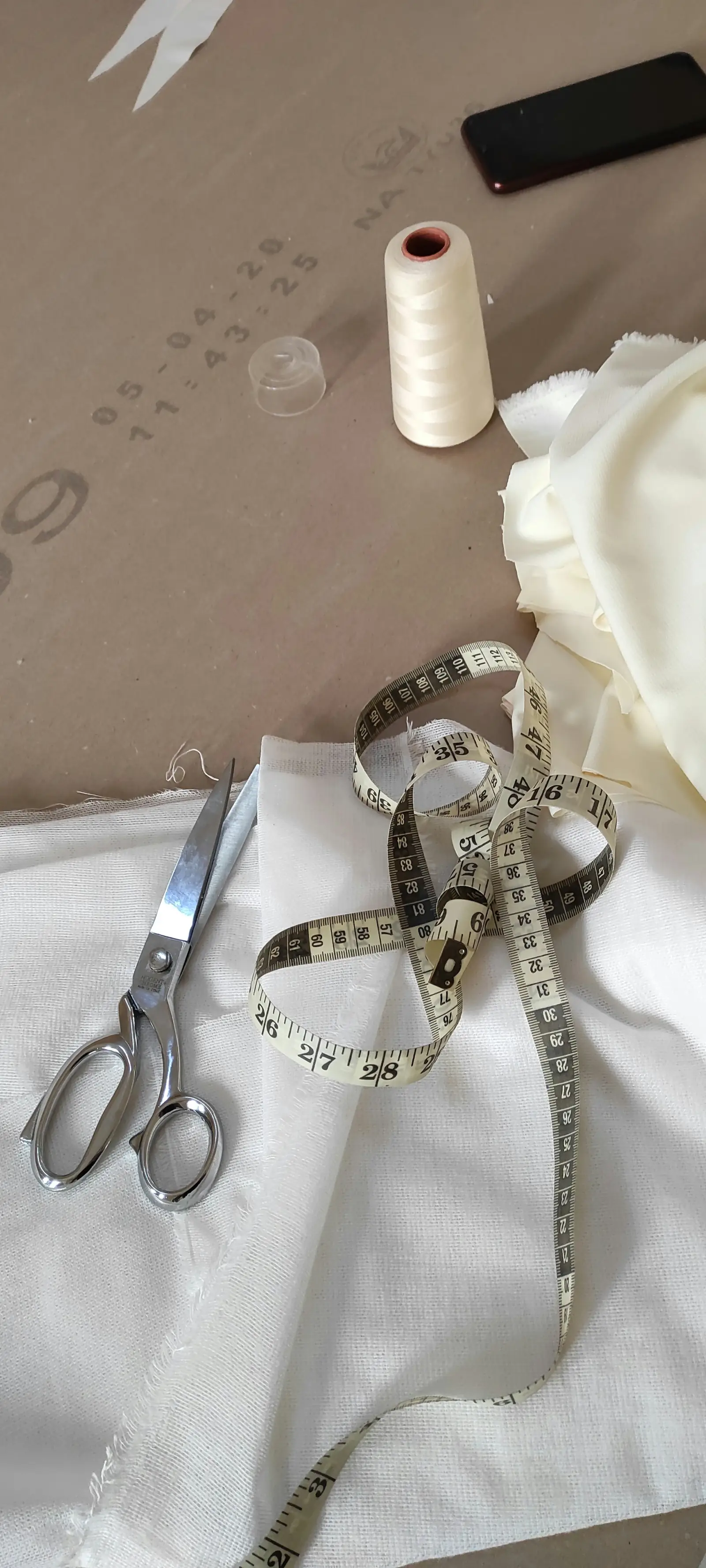 Tailoring scissors, a measuring tape and a spool of thread resting on white cotton fabric