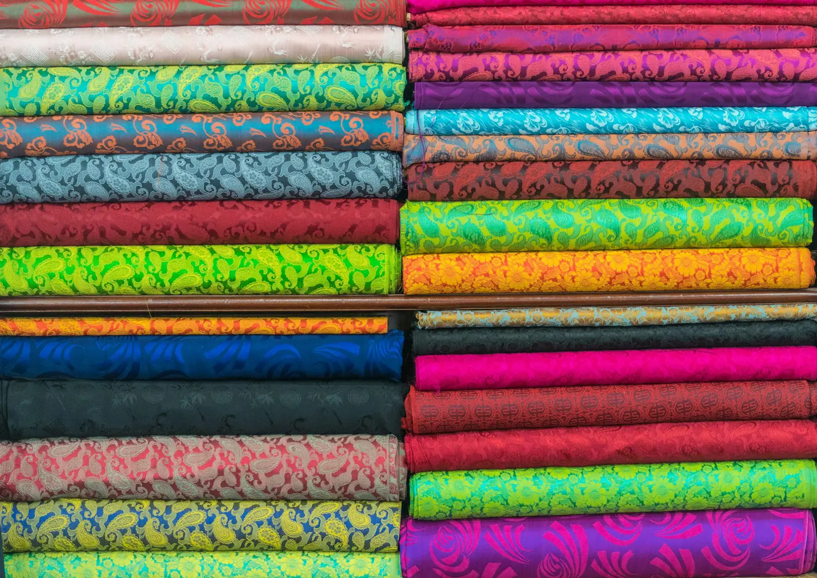 Neat stacks of folded patterned fabric in bright pinks, greens, blues and oranges on shop shelves
