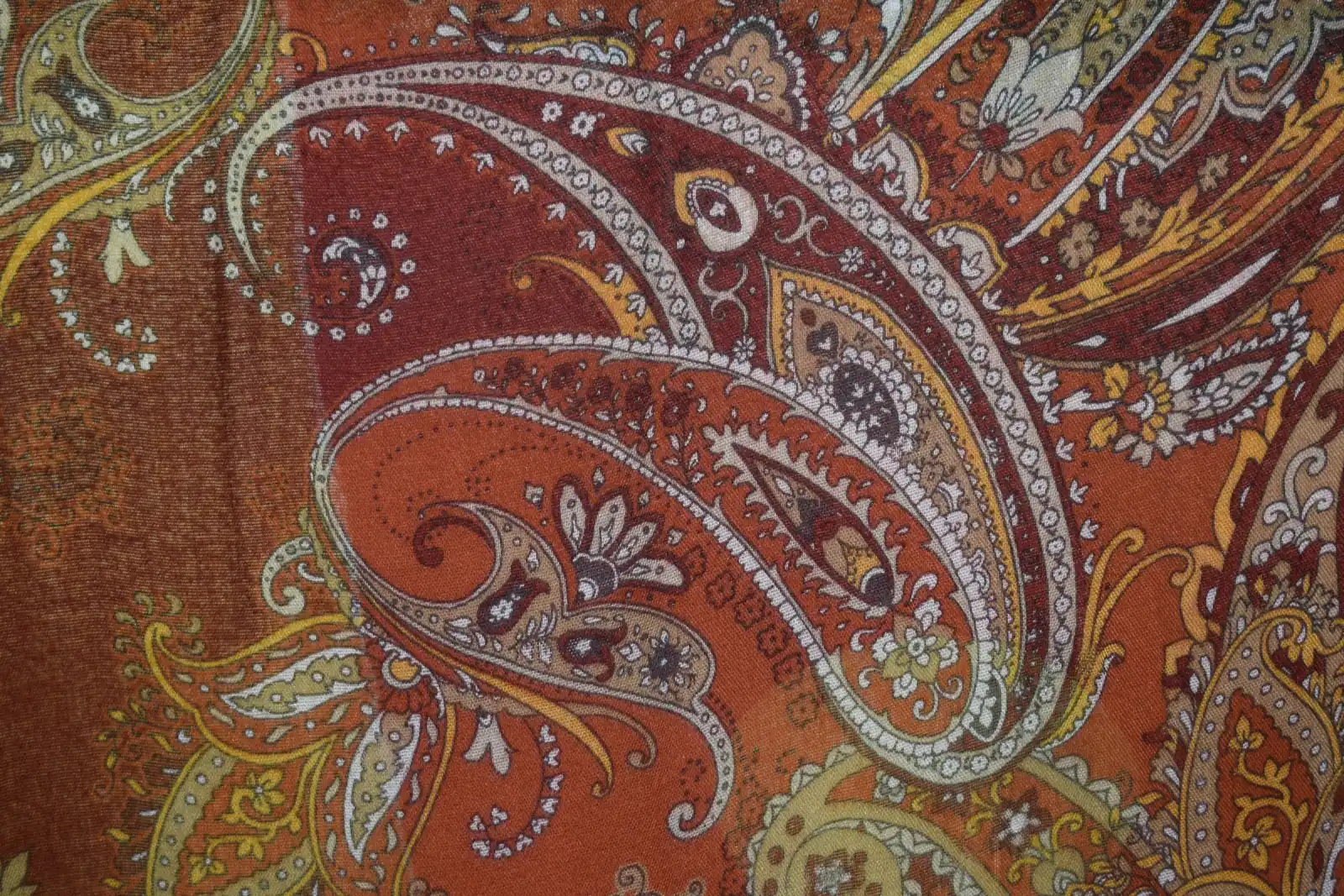 A close-up of a paisley print fabric in rust, gold and cream with ornate curling motifs