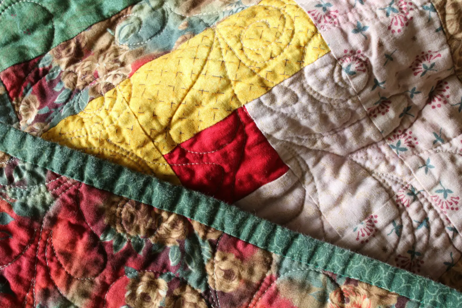 Close-up of a hand-quilted cotton quilt with floral patches, yellow and red blocks and a green border
