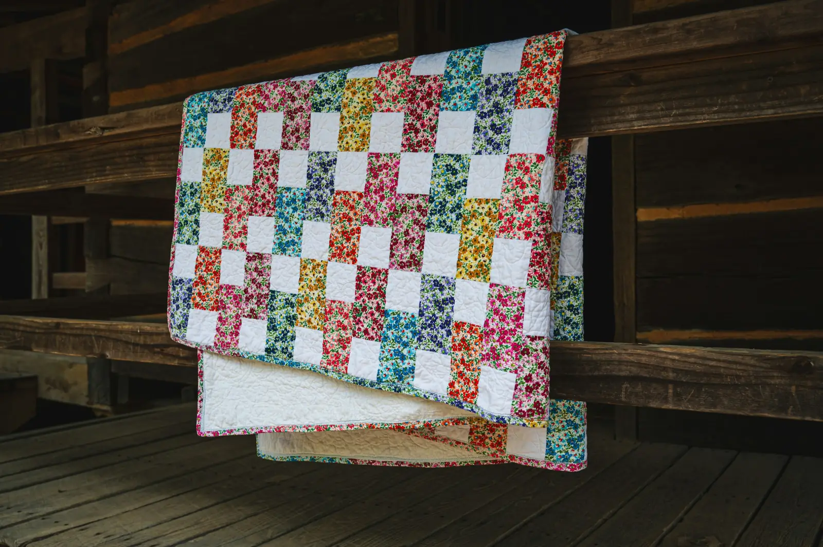 A finished patchwork quilt with small floral squares folded over a wooden railing