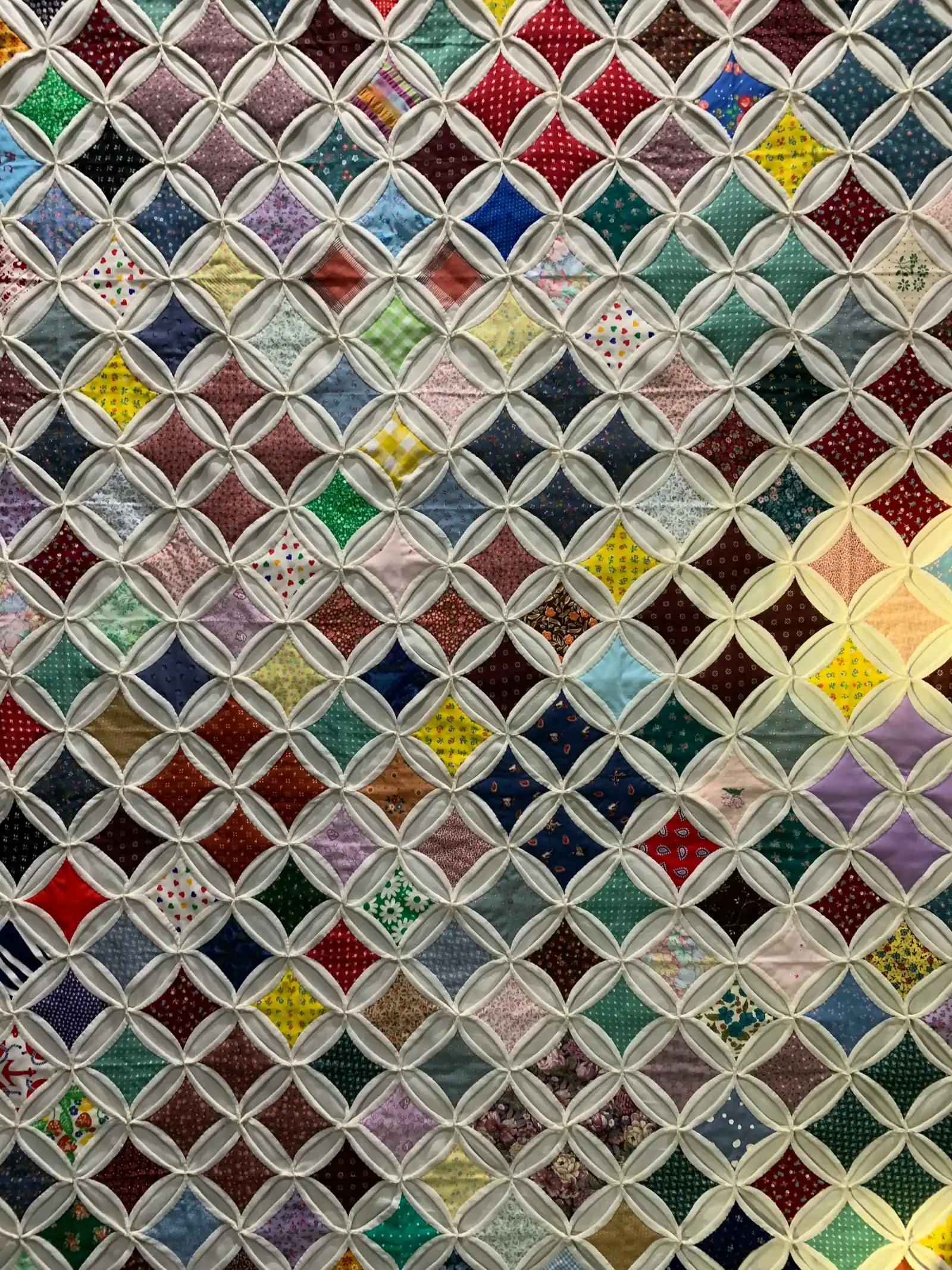 A patchwork quilt made of dozens of small coloured squares set in a white lattice of stitched curves