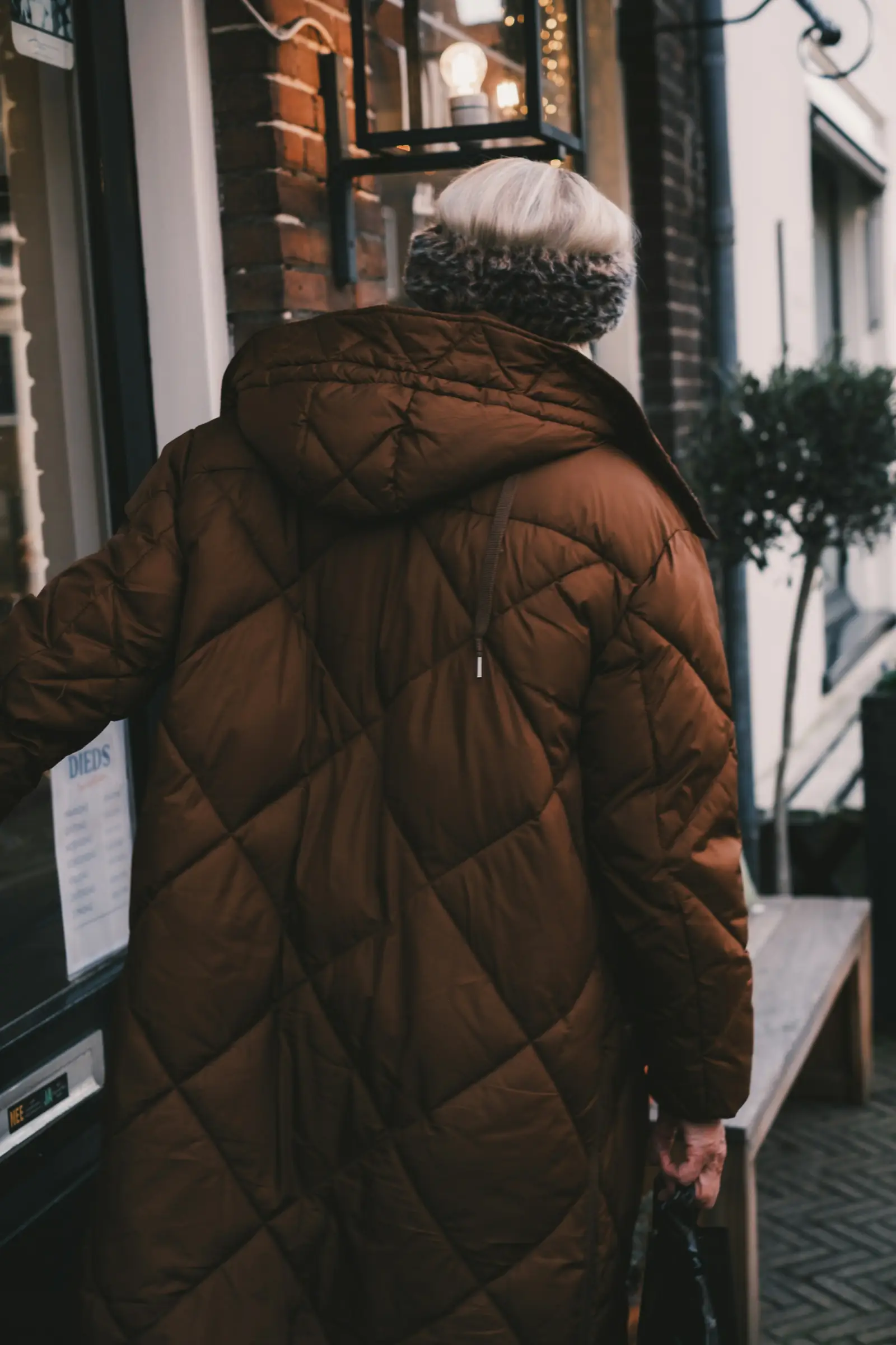 A person in a long brown quilted winter coat walking into a building on a cold day