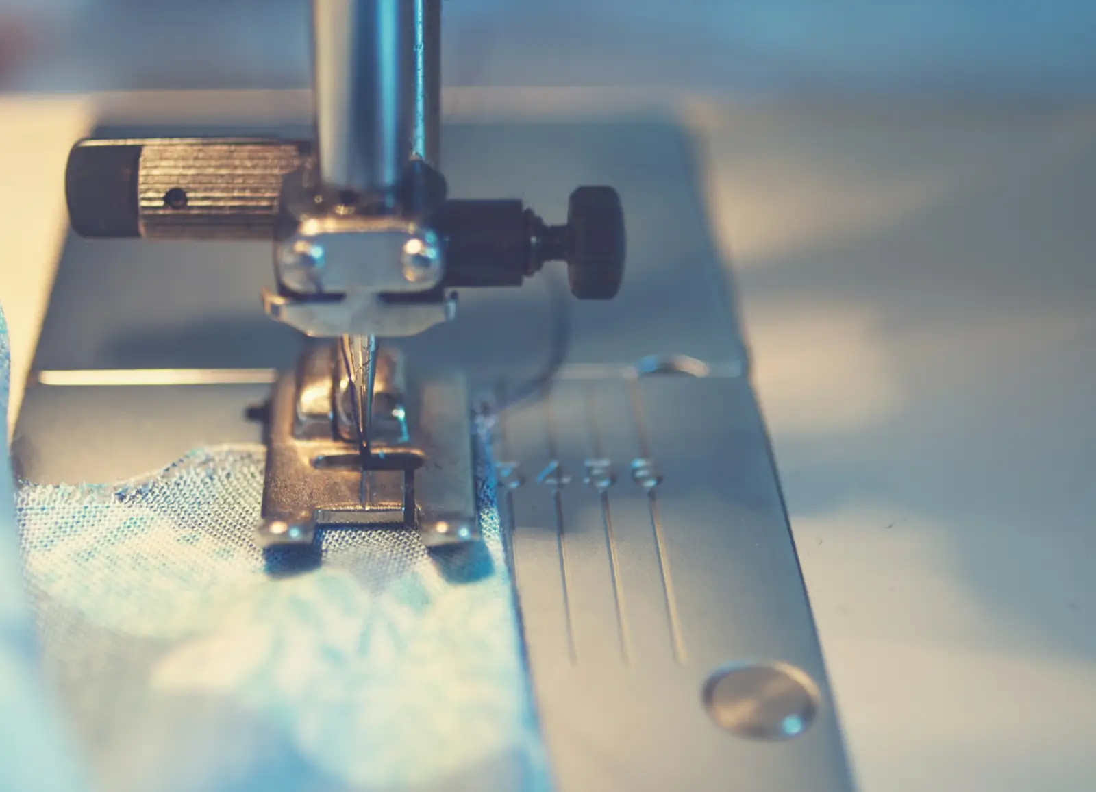 Close-up of a sewing machine needle and presser foot stitching through layered fabric