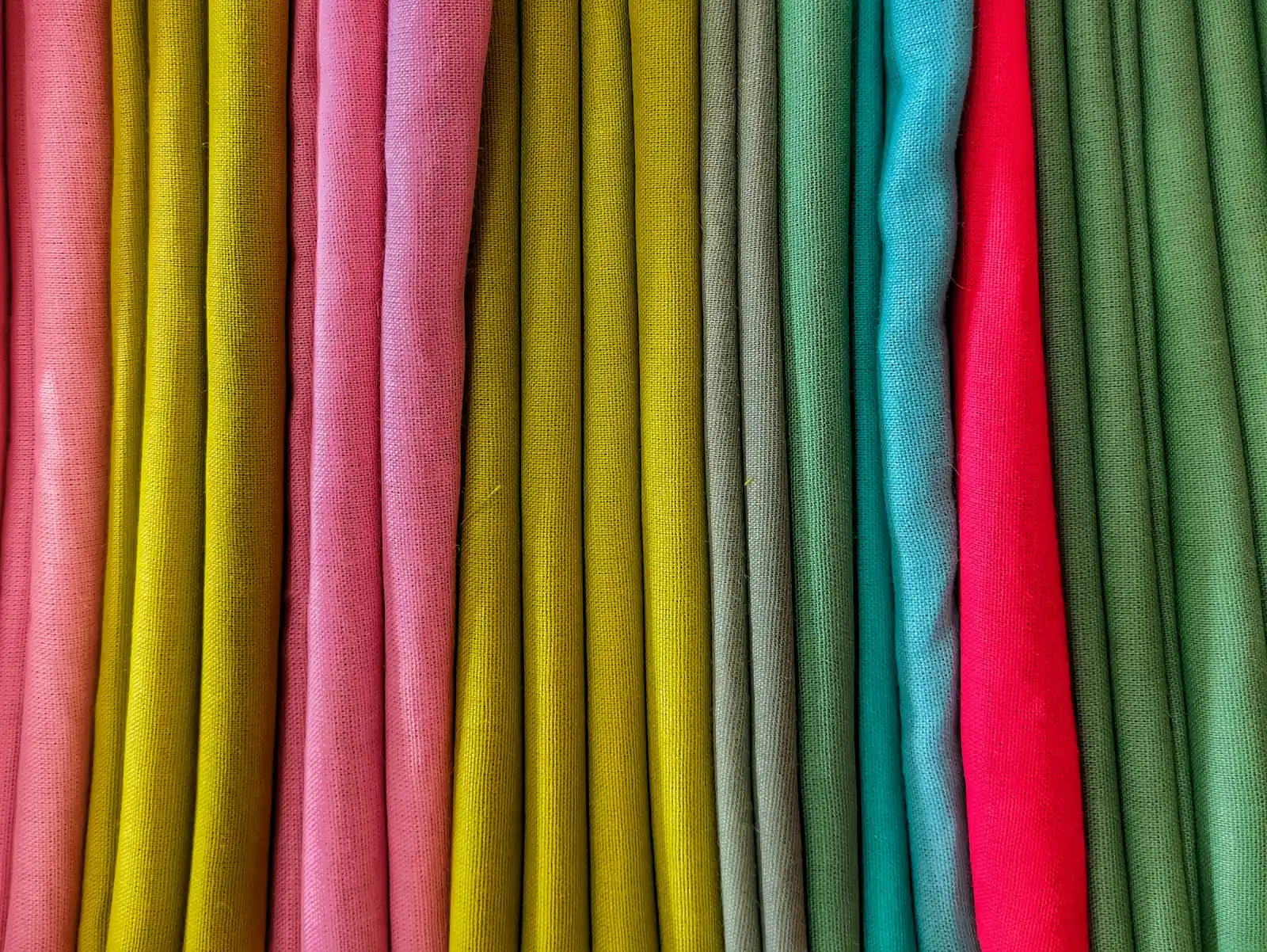 Folds of plain cotton fabric in pink, mustard, olive, teal and green hanging side by side