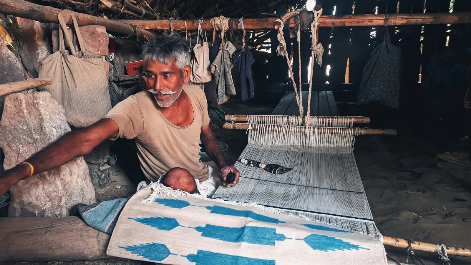 A weaver working a patterned textile on a traditional wooden handloom in India