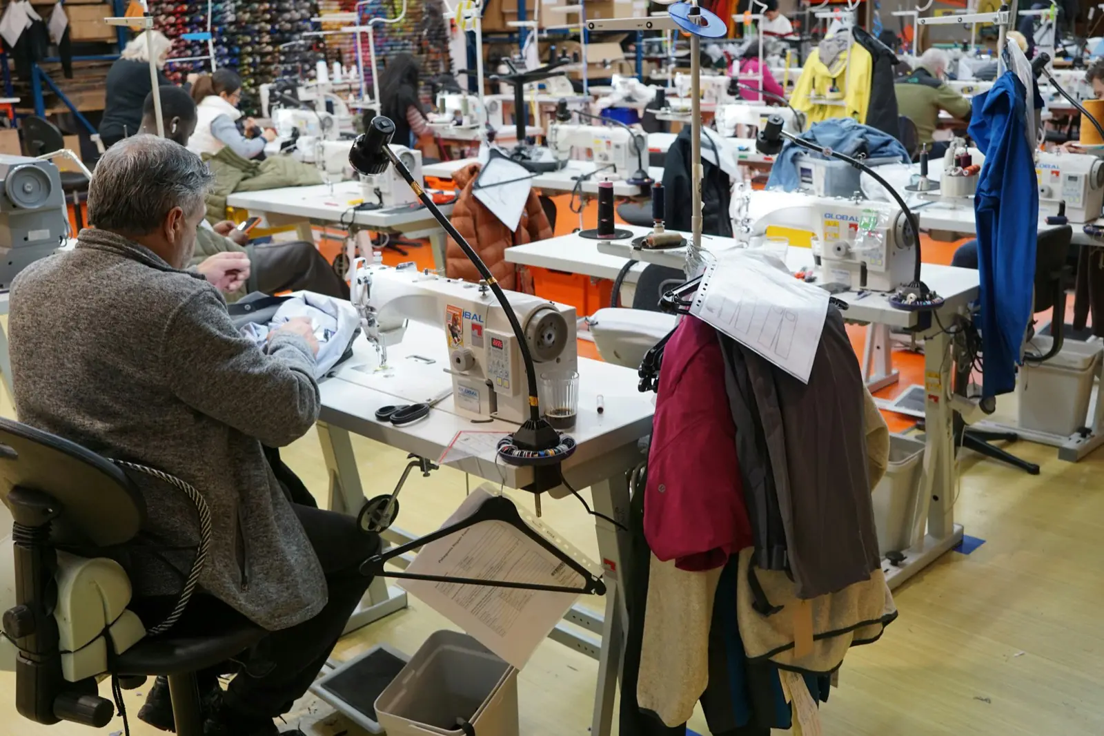Tailors working at rows of industrial sewing machines in a garment workshop