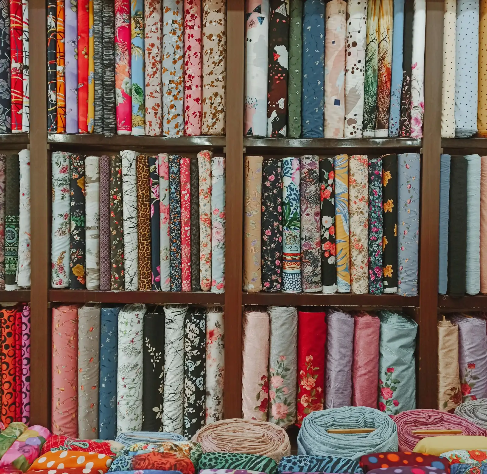 Tall wooden shelves in a fabric shop packed with upright rolls of printed cotton in many colours