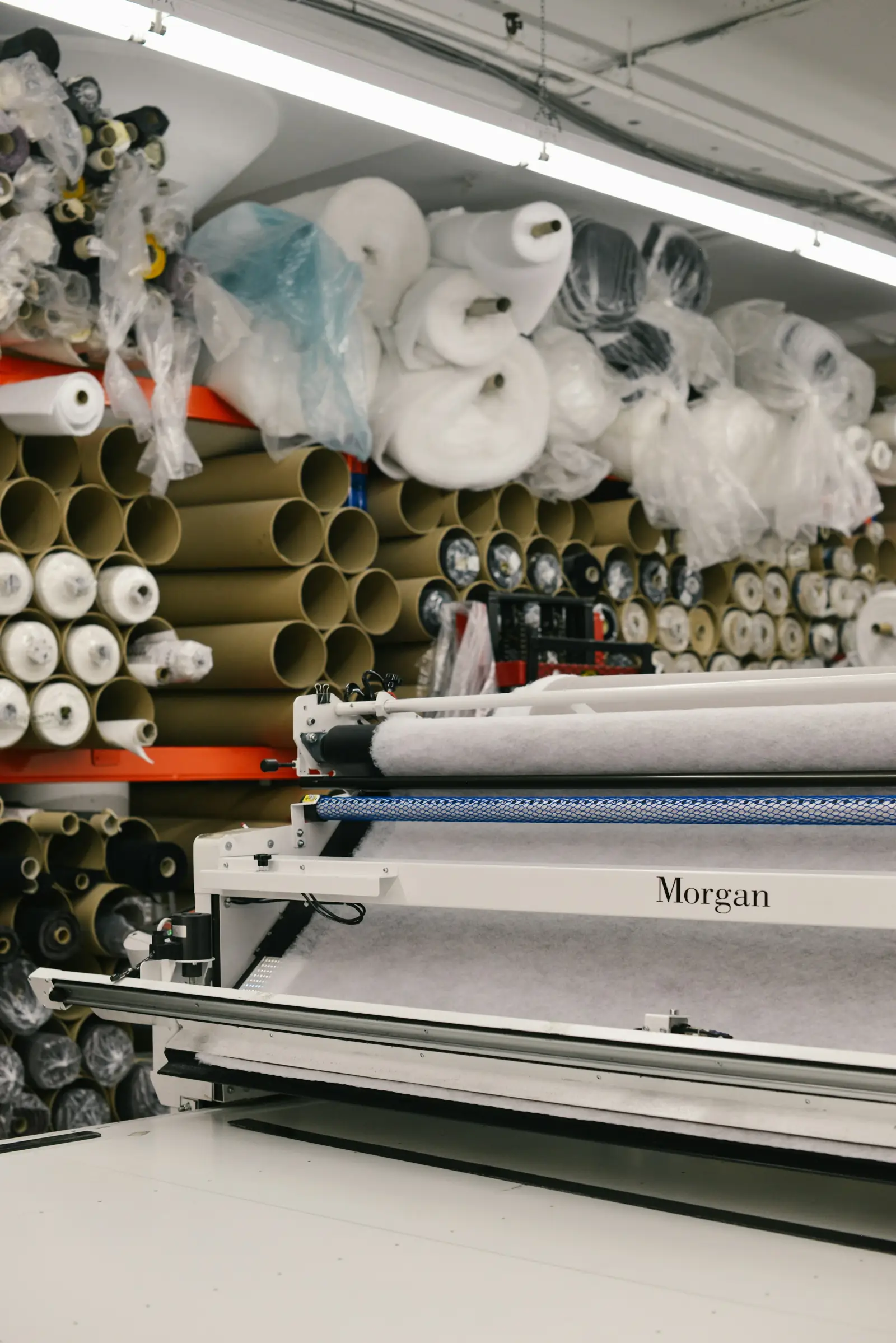 A textile workroom with racks of large fabric rolls on tubes behind a long cutting table