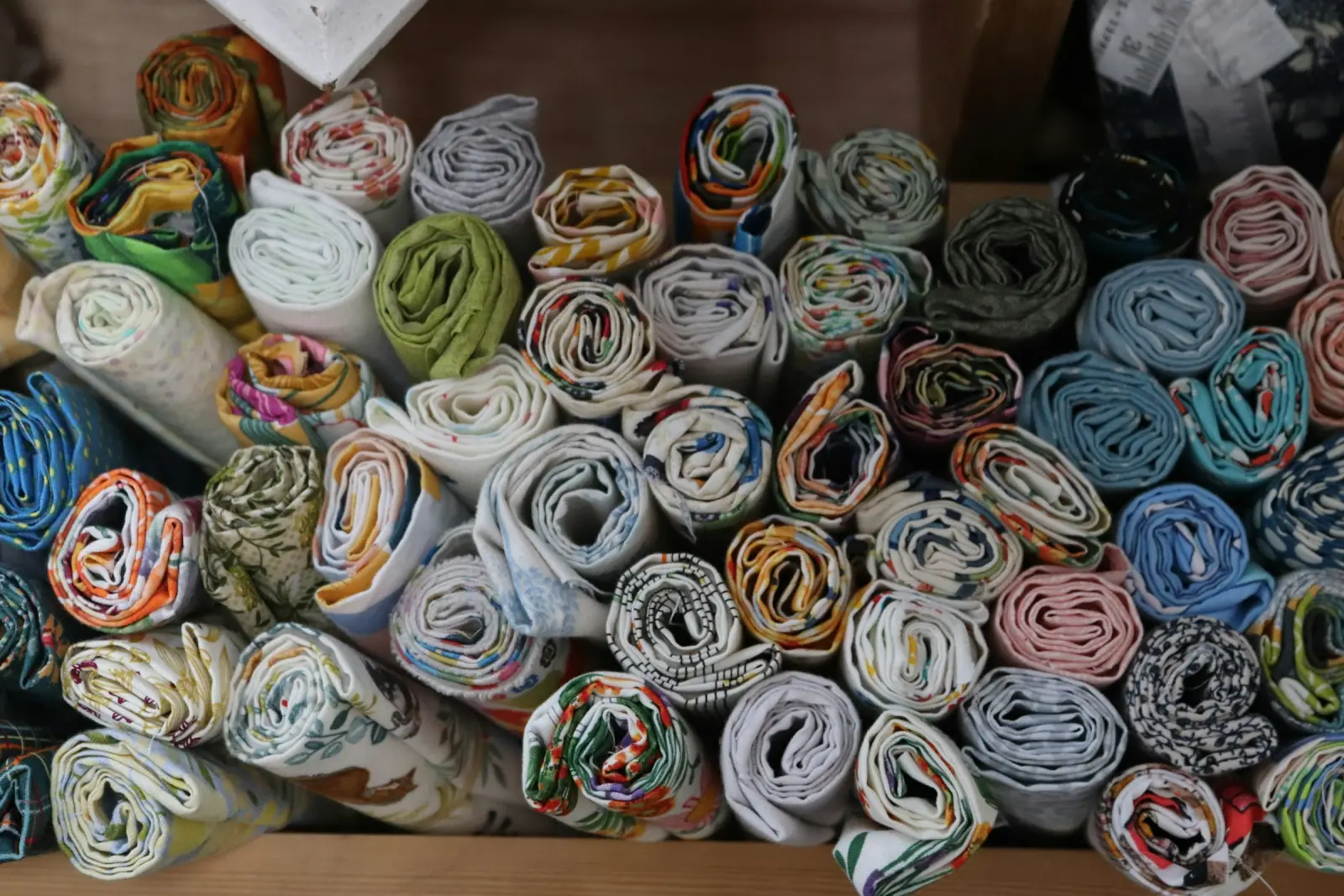 A jumble of rolled printed cotton fabrics piled together on a shelf, seen end-on