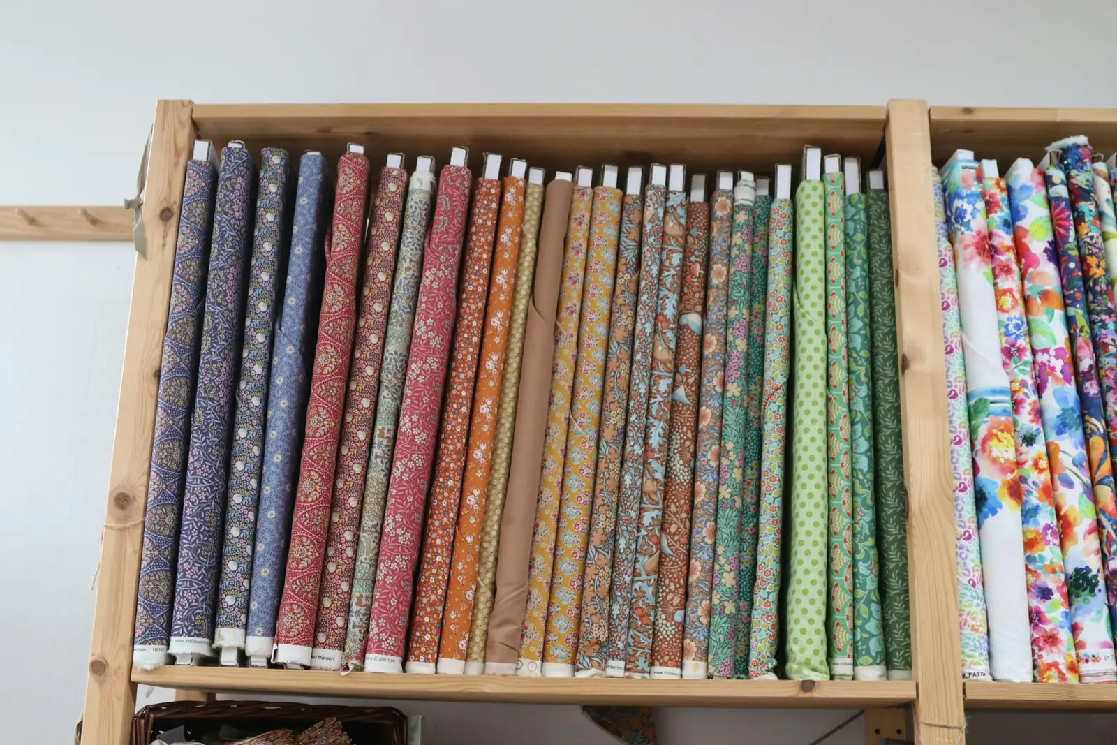 A wooden shelf holding rolls of patterned cotton fabric standing upright side by side