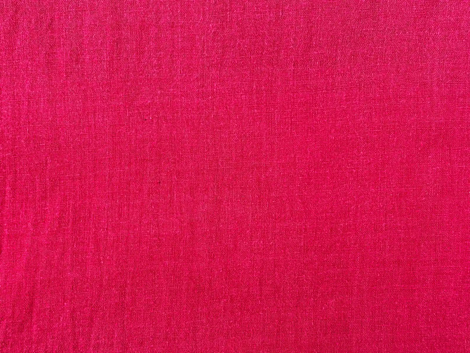 A close-up of plain raspberry red woven cotton fabric with a slightly textured weave