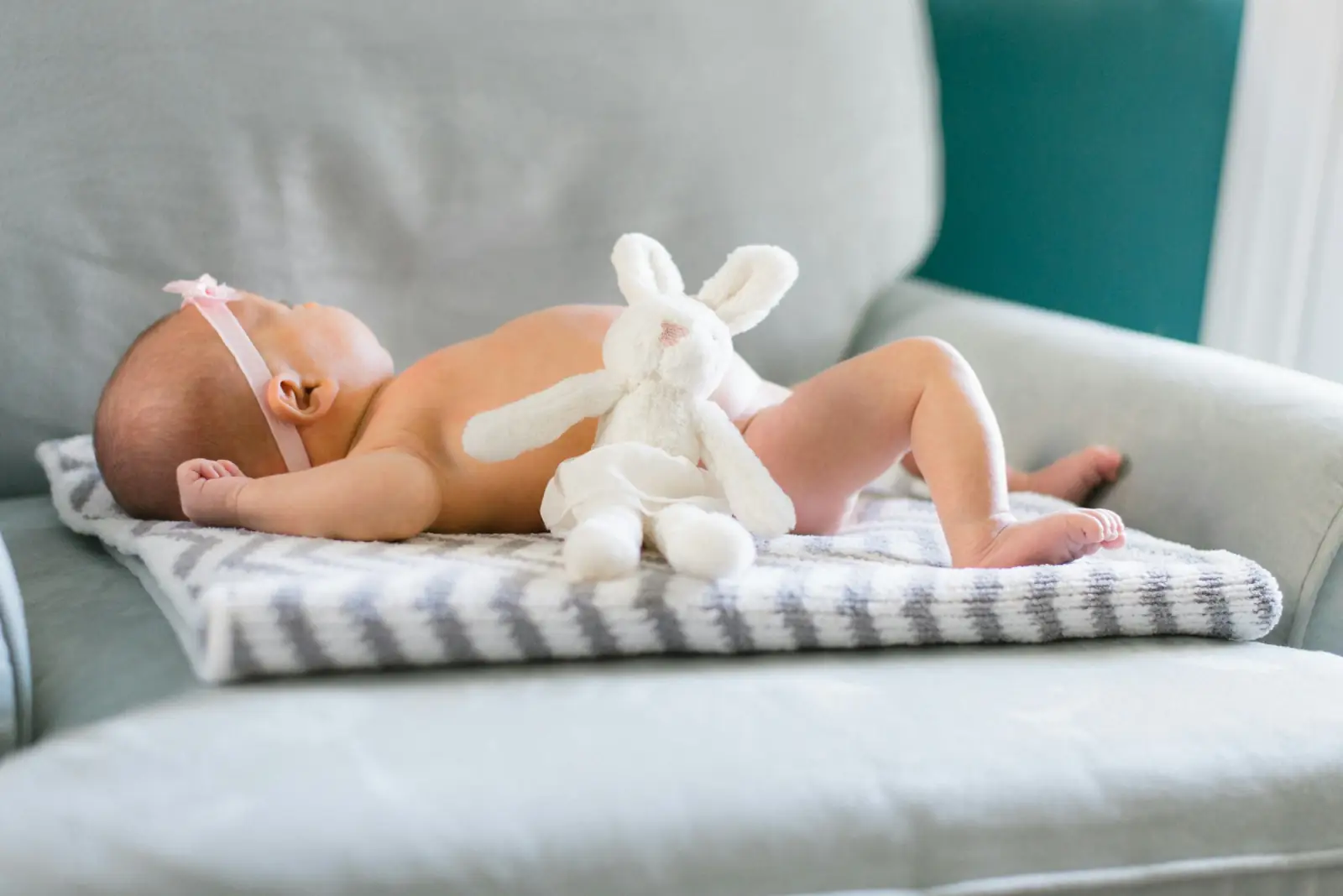 A newborn baby lying on a soft striped blanket on a sofa, holding a white toy rabbit