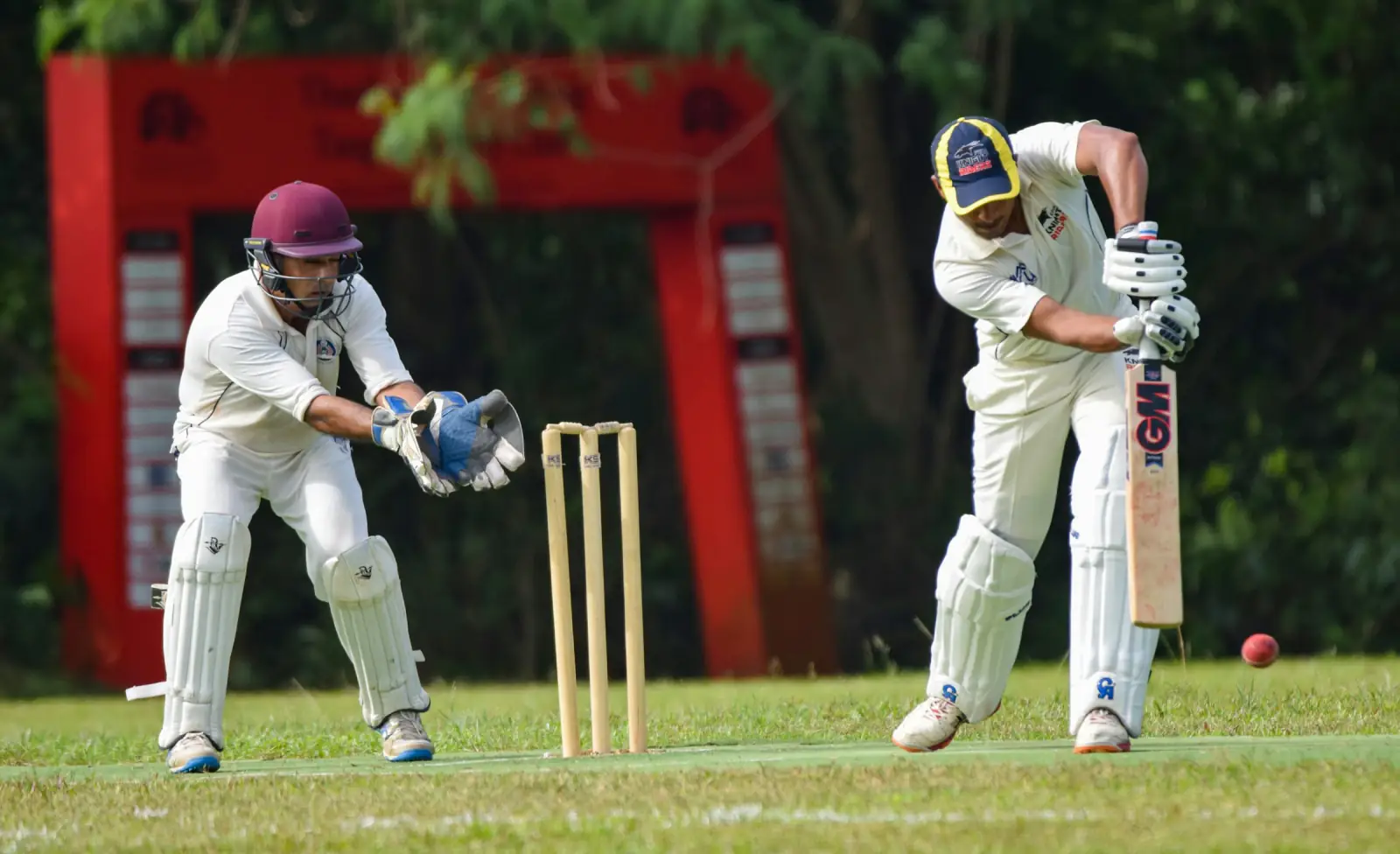 A batsman and wicketkeeper in white cricket clothing during a match, with the stumps between them