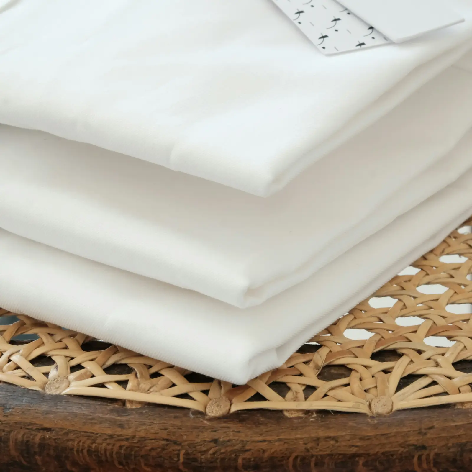 A neat stack of folded white cotton fabric resting on a cane basket