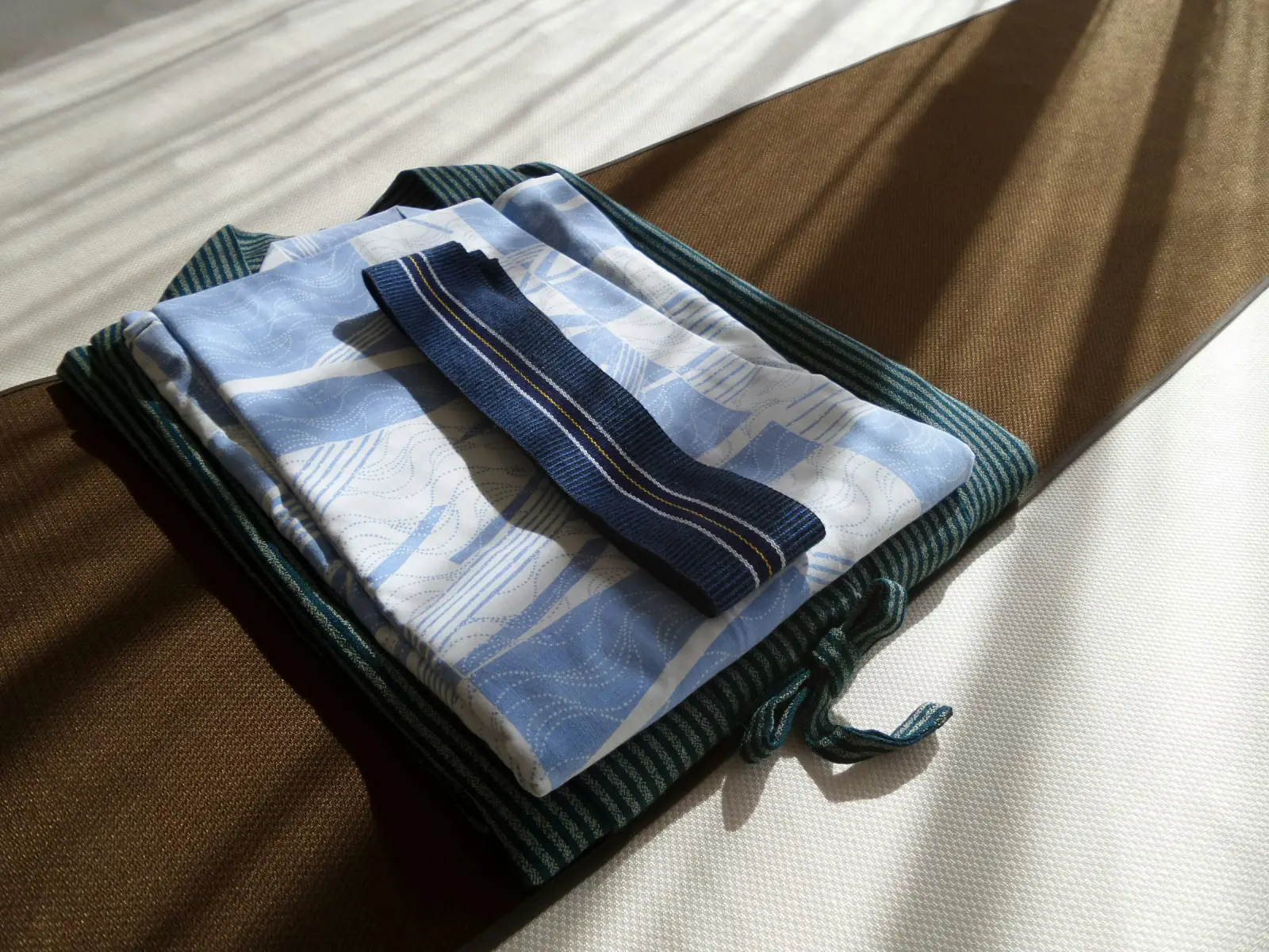 A folded set of light blue checked cotton nightwear with a dark trim on a bed