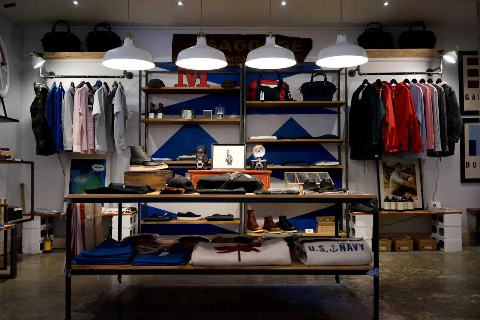 A menswear shop interior: folded stock on a central display table, shirts and jackets on rails behind